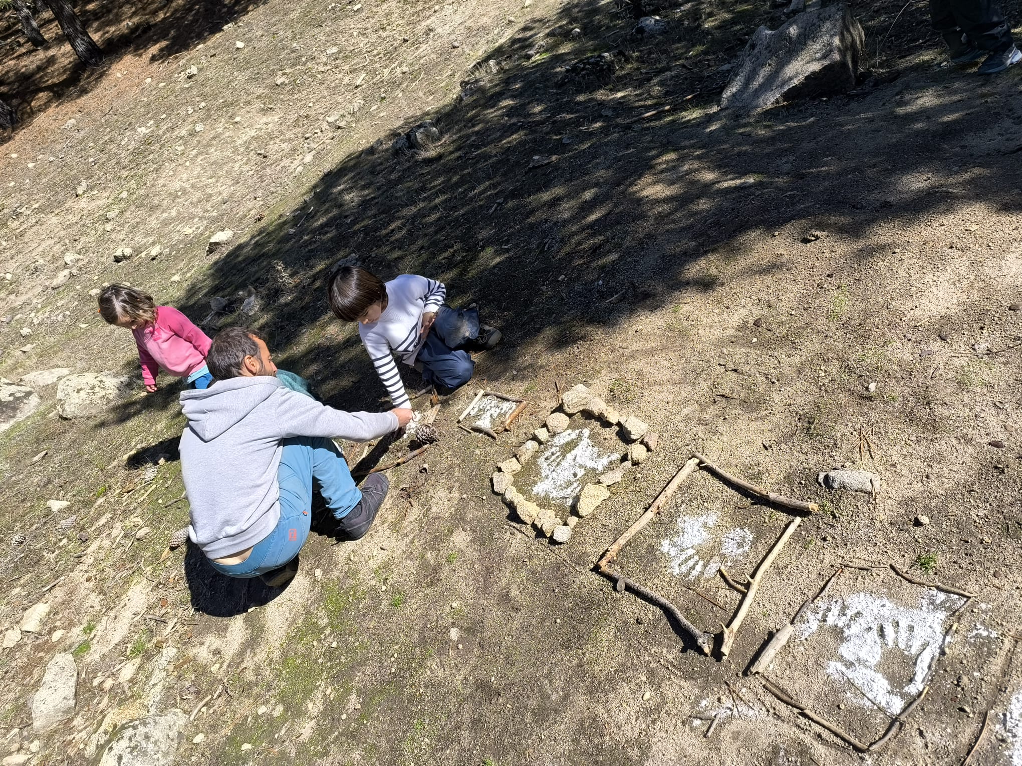 Un adulto acompaña a dos niños mientras crean con elementos naturales en el bosque